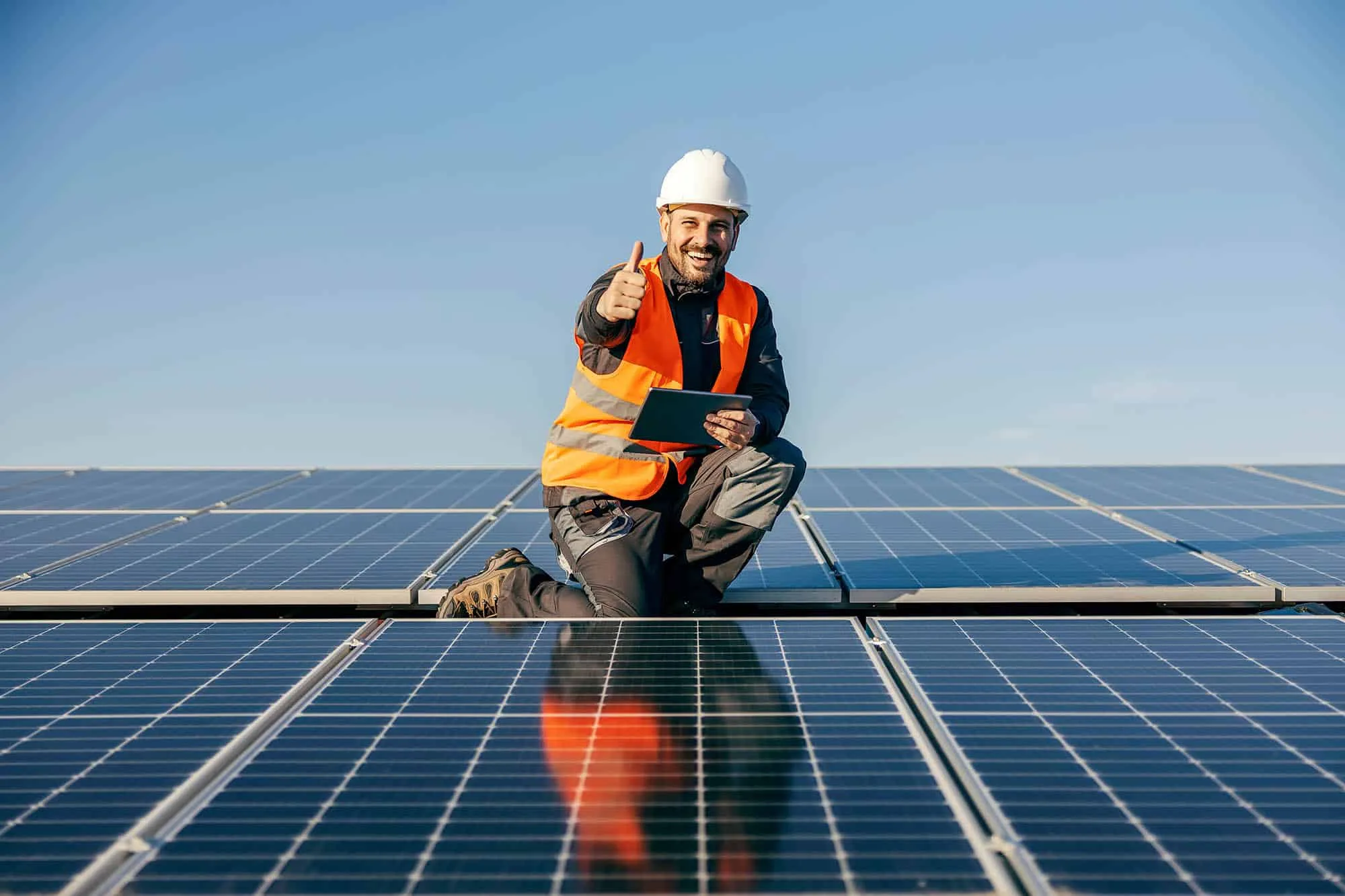 A solar technician on a roof smiling while posing for the camera.