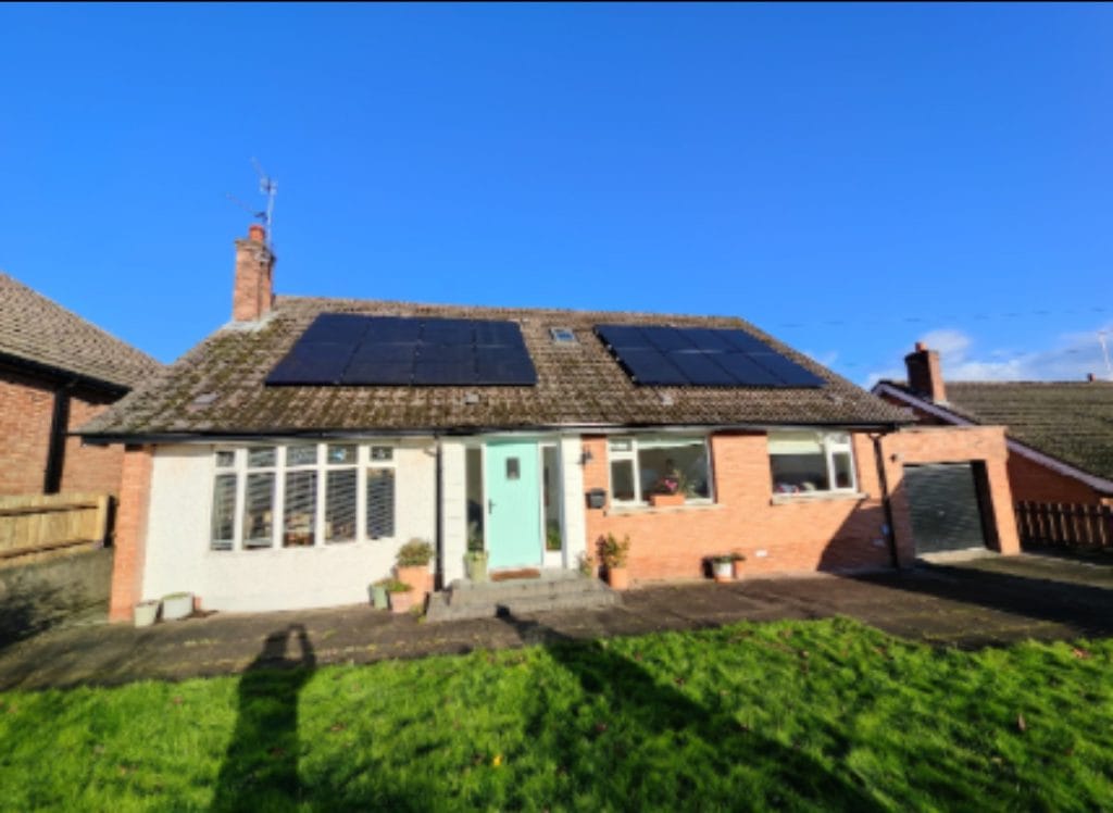 Residential building with solar panels installed on the roof, featuring a light blue front door and landscaped garden.
