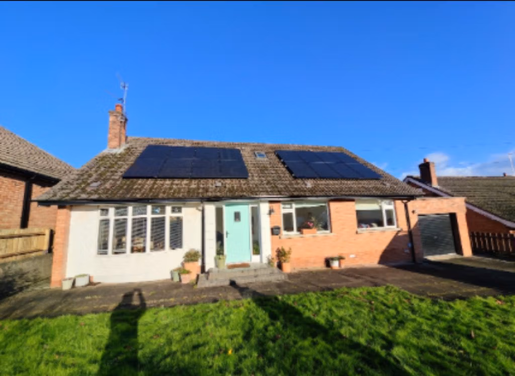 Residential building with solar panels installed on the roof, featuring a light blue front door and landscaped garden.