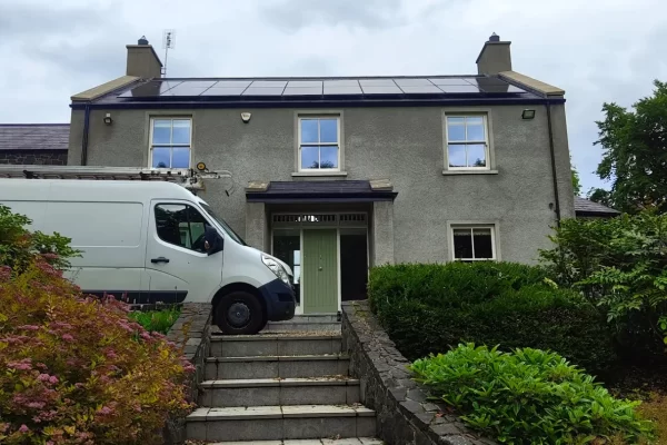 Residential building with solar panels installed on the roof, featuring a van parked in front and a landscaped pathway leading to the entrance.